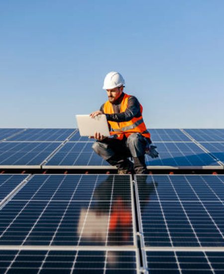 A handyman looking at the laptop on rooftop and testing solar panels.